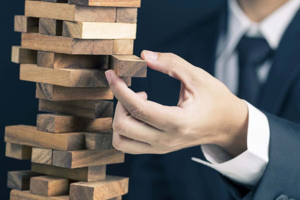 man in business suit pulls a piece out of wobbly wooden tower